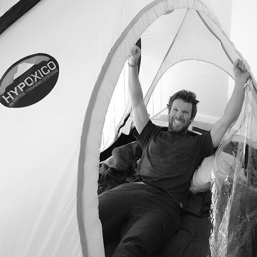 A man with a beard smiles broadly with his arms raised, lying inside a