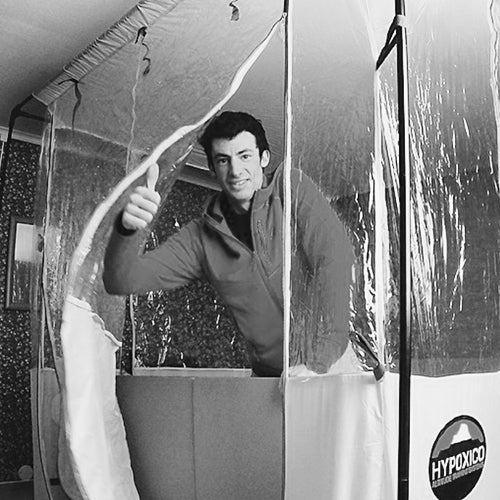 A man giving a thumbs up from inside a clear, sealed hypoxic tent with a